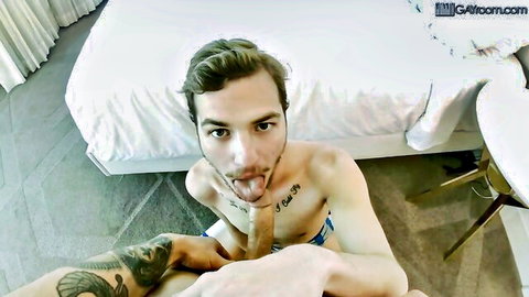 Tattooed young man sticking tongue out while handling yellow dildo in shorts