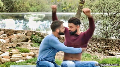 Latino gay lovers embracing intimately outdoors by lake, Falcon Studios