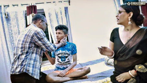 Indian man gently holding young boy's face while woman in black saree watches clothed taboo scene