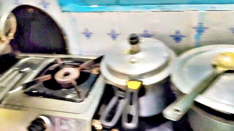 Blurry homemade South Asian kitchen stove with silver pressure cookers and yellow ladle on blue tiles