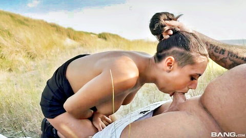Tanned brunette babe with natural tits sucks huge cock outdoors on grassy beach