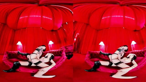 Brunette in black lingerie and thigh-high boots straddles partner on pink couch in red VR room