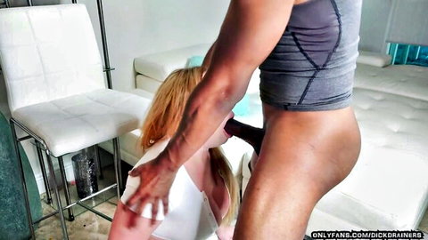 Blonde woman on knees deepthroating muscular black man's huge erect cock in intense blowjob.