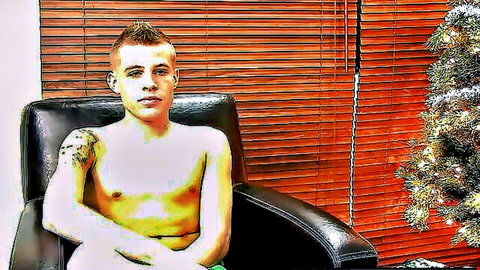 Shirtless young tattooed gay hunk sits teasingly in leather chair by Christmas tree