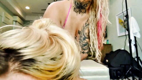 Tattooed busty blonde in pink bikini leans over in steamy threesome setup