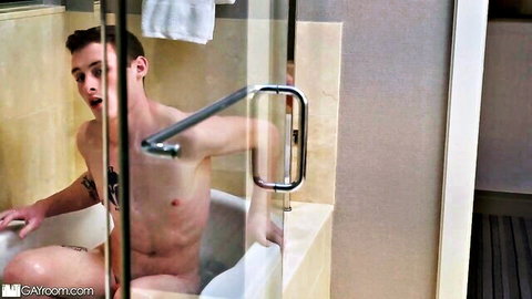 Surprised naked young twink with tattoos sits in steamy bathtub shower exposing toned body