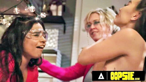 Blonde MILF and busty Asian babes topless embracing in lesbian kitchen play with goggled teen