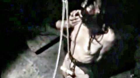 Retro BDSM scene: bound topless woman suspended in ropes, blindfolded torture