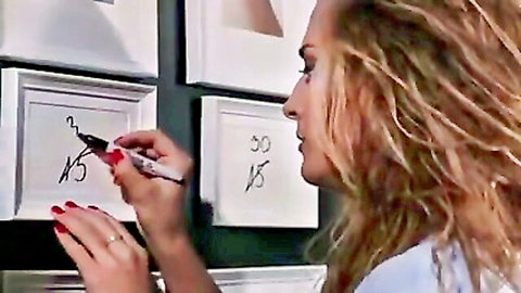 Blonde woman with red nails writing numbers on white gallery frames