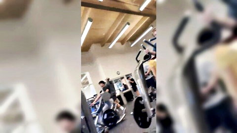 Blurry PAWG in tight shorts rides exercise bike in crowded gym with fit guys