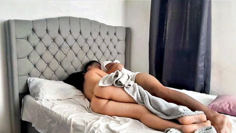Nude woman with big ass lying face down in bed as naked man spoons her from behind intimately