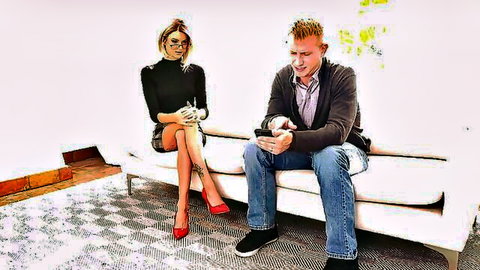 Petite blonde with glasses in black skirt and red heels eyes guy checking phone on couch
