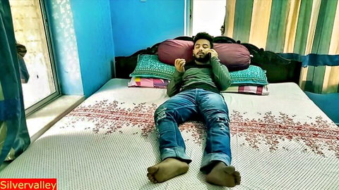 Desi Indian man lying on bed in apartment wearing jeans and shirt selfie