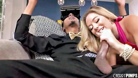 Blonde babe in pink dress teases suited guy's crotch with hand while he wears VR headset smiling on couch