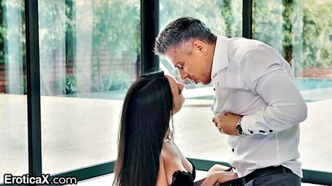 Suited grey-haired man passionately kissing brunette's neck and groping her cleavage in black lace bra