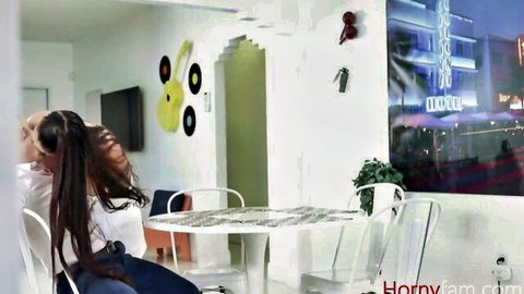 Curvy long-haired brunette MILF in white top sits at table with sexy friend in neon Vegas room