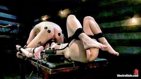 Two naked bound women with electro pads on asses and pussies in BDSM restraint