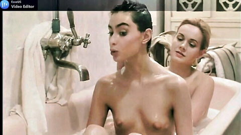 Two topless young women with perky tits in steamy bathtub, short-haired brunette leans forward with open mouth