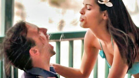 Tanned brunette in turquoise bikini spits into laughing man's open mouth on porch