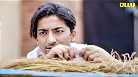 Intense desi man in white shirt peeking through hay with gripping hands and stern gaze
