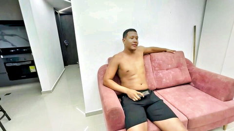 Muscular shirtless black guy lounging in black shorts on pink couch with bulge tease