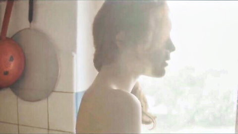 Topless blonde woman in kitchen, side profile bare back view