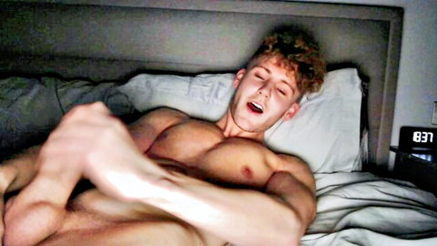 Muscular curly-haired guy masturbating intensely on bed