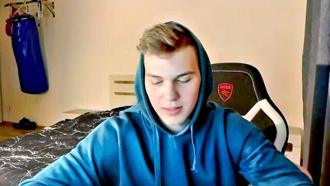 Cute twink gamer boy in blue hoodie sits in gaming chair on webcam