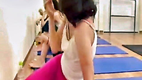 Japanese fitness instructor in white tank top and pink leggings leading yoga class