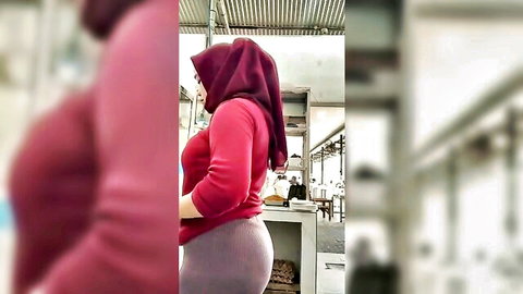 Curvy hijab woman in red top and tight gray pants posing in kitchen