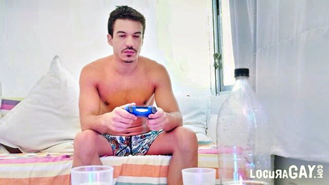 Shirtless muscular gay hunk with mustache plays video game controller on bed in colorful shorts