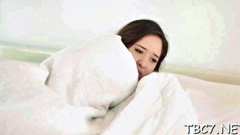 Teary-eyed Asian beauty peeking from white sheets in bed, softcore tease