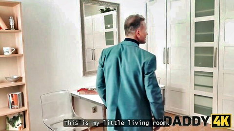 Suited mature DILF daddy standing in modern living room with daddy4k text overlay