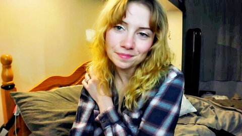 Smiling blonde babe in plaid flannel shirt sitting on bed teasing seductively