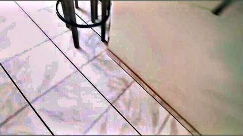 Blurry closeup of shiny white tiled floor with metal bar stool legs and reflections