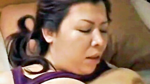 Chubby Japanese MILF in purple top, eyes closed in pleasure on bed