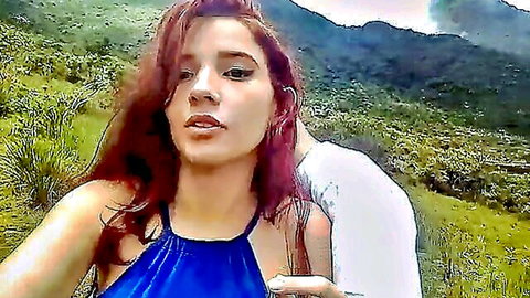 Young redhead Latina girlfriend in blue halter top hugged by boyfriend outdoors in mountains