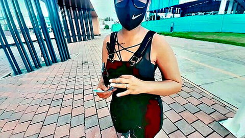 Young woman in sexy black harness dress, Nike mask, sunglasses outdoors holding phone