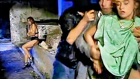 Brunette in black lingerie spreads legs wide on stone ledge as man grabs blonde's head in vintage group tease