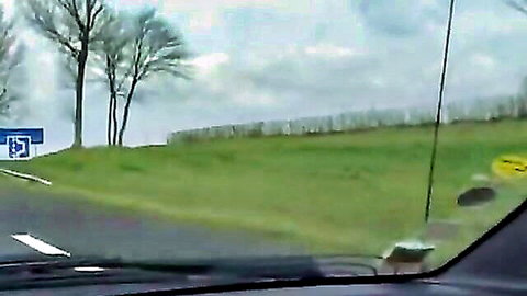 Dashboard view of rural road with green hill, trees, and directional signs in France