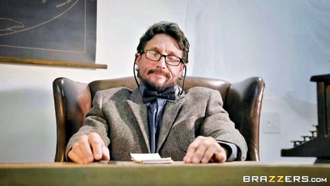 Bearded professor in tweed suit and glasses sits at desk in classroom office
