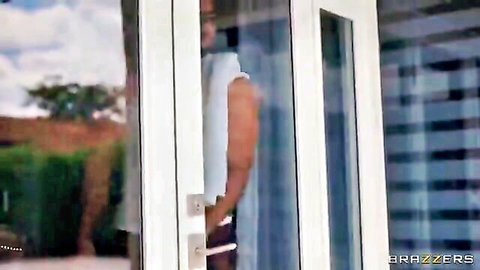 Muscular man in white shirt stands by glass door in sunny backyard outdoor scene