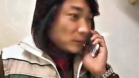 Young East Asian guy with long black hair in hoodie talking intently on flip phone