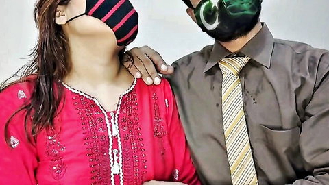Sexy South Asian wife in red salwar kameez smiles with masked Pakistani husband arm around her shoulder