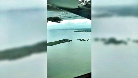 Blurry aerial view from airplane window over turquoise ocean with small islands and plane wing visible