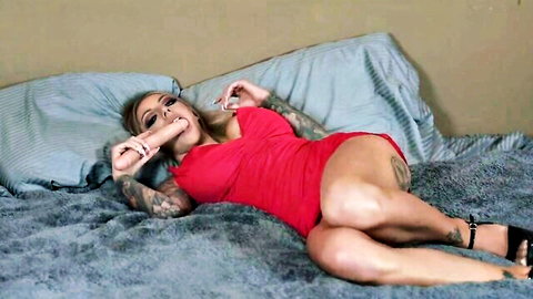 Tattooed blonde in red dress sucking dildo seductively