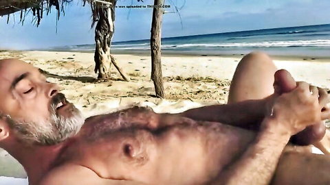 Bald hairy daddy stroking his cock on sunny beach by ocean