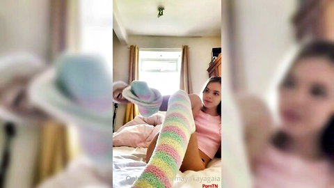 Cute Asian teen in pink top and striped knee socks lifts foot teasingly on bed for foot fetish