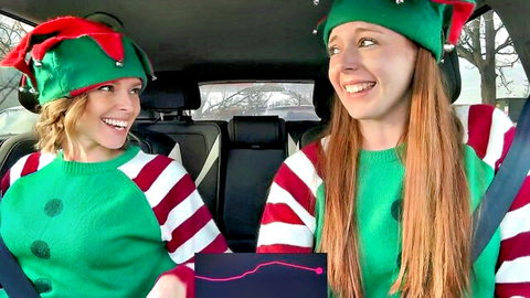 Two sexy elf girls smiling in car backseat wearing festive green sweaters