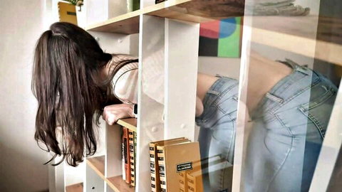Brunette babe bending over bookshelf with jeans pulled down exposing bare ass cheeks